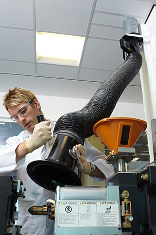 Student in labcoat holding a hose originating from the ceiling