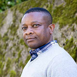 Student wearing checked shirt under grey sweater smiles at the camera.