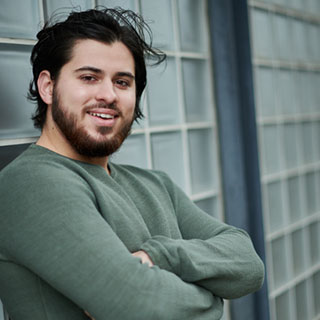 A student smiling at the camera and leaning on a patterned wall.