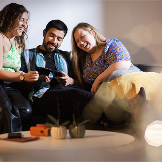 Three students sat together on a sofa, smiling whilst looking at photographs.