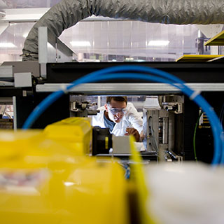 A lab technician wearing goggles working infront of lab equipment.