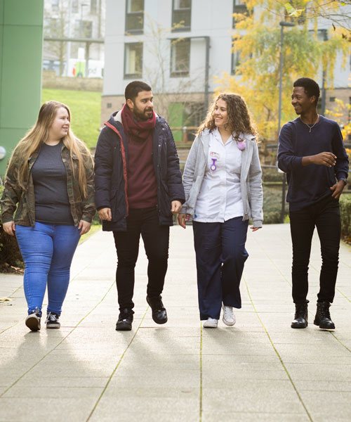 Four smiling students walking towards the camera.