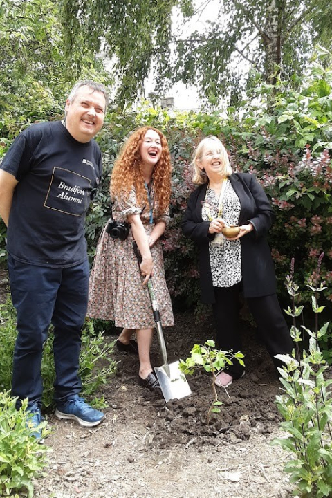 Three people stand smiling in a wood.