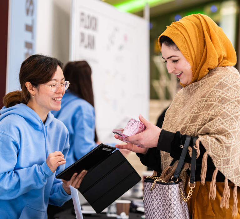 A University of Bradford staff member and student look at a phone while smiling.