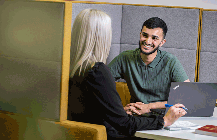 Two social work students chatting in a booth and smiling.