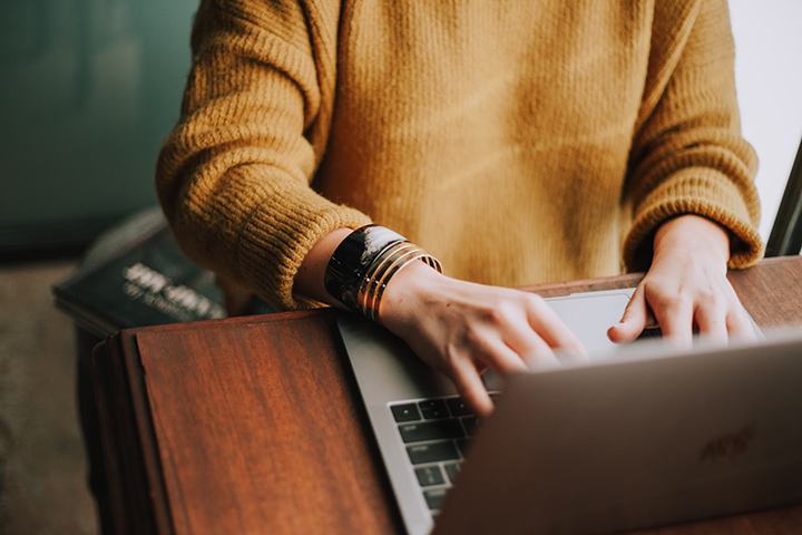 Person wearing a yellow jumper typing on a macbook