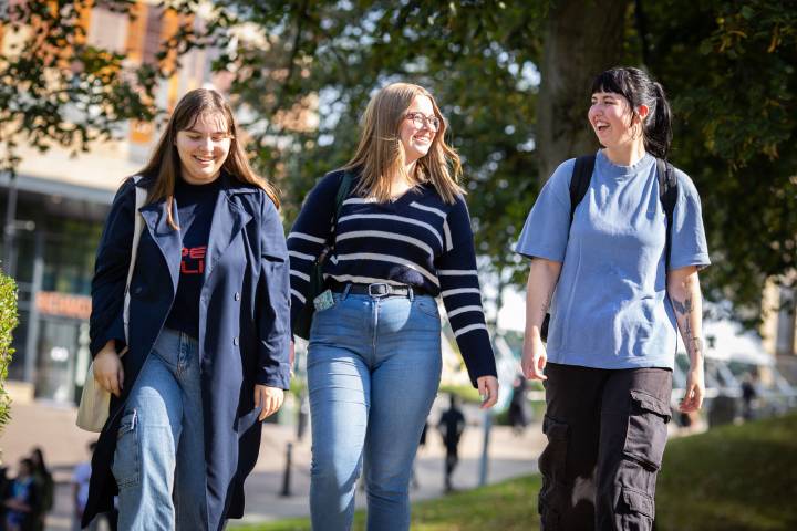 Three students smile and chat while walking in the sunshine.