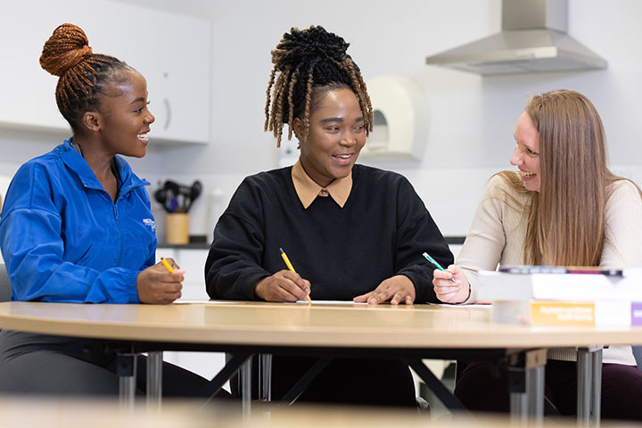 3 nursing students sitting round a table, chatting and making notes.