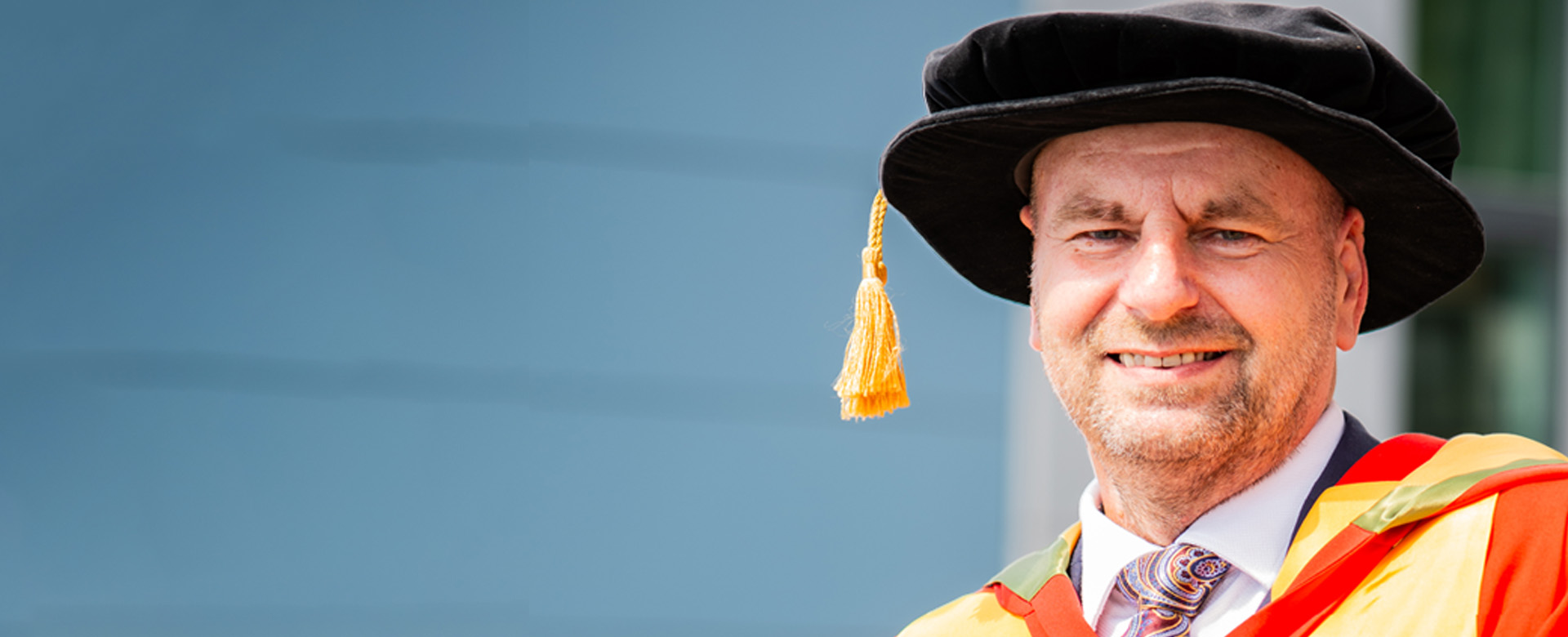 Honorary Graduate Alan J Banks, posing in Richmond Building wearing red and gold graduation gowns.