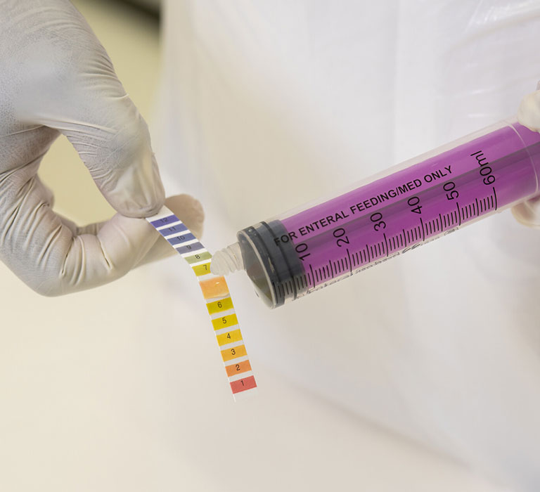 Syringe with coloured liquid measured against PH paper strip