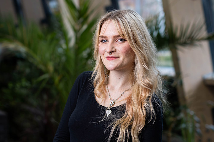 Molly, Public Health and Community Wellbeing student, smiling at the camera in a room decorated with foliage.