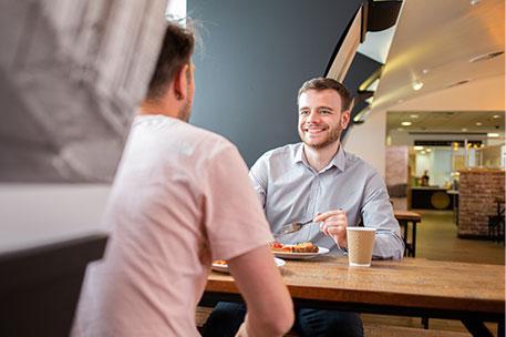 Two students chatting whilst eating food.