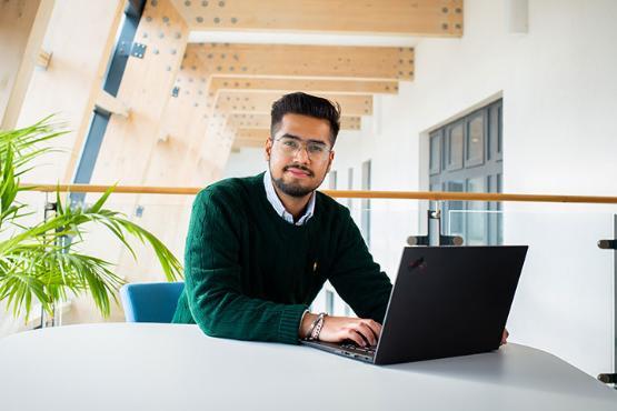 A postgraduate student sitting at a desk with their laptop.