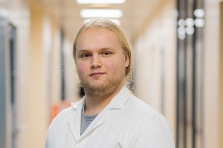 A student wearing a lab coat smiling at the camera