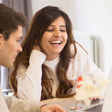 Two students laughing over a laptop.