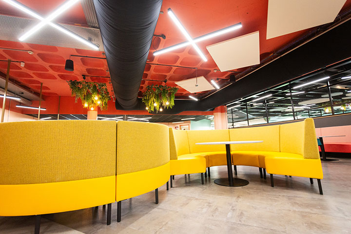 An empty well lit seating area decorated with a yellow curved sofa