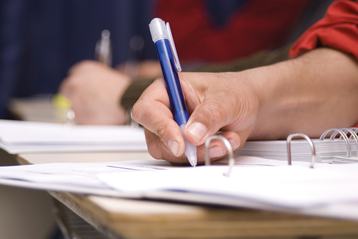 A student writing notes with a blue pen