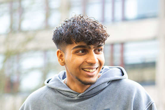 A student sitting outside on the University of Bradford campus, smiling and looking into the distance