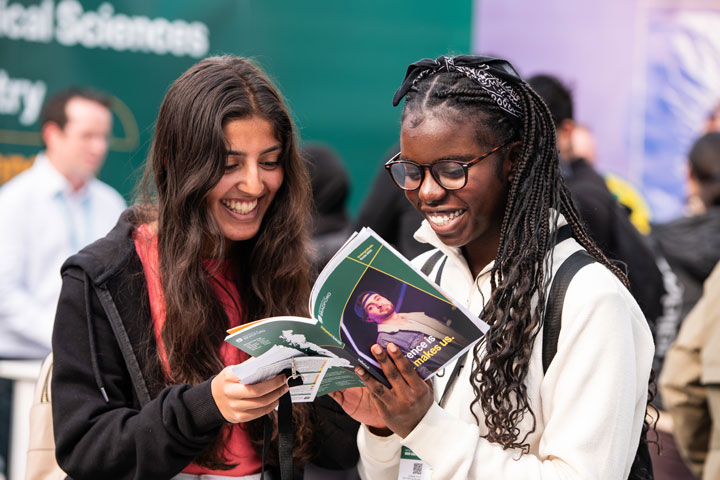 Two prospective students at a University of Bradford Open Day smiling and looking at the prospectus