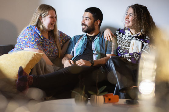 Three students sitting on a sofa smiling and chatting with each other
