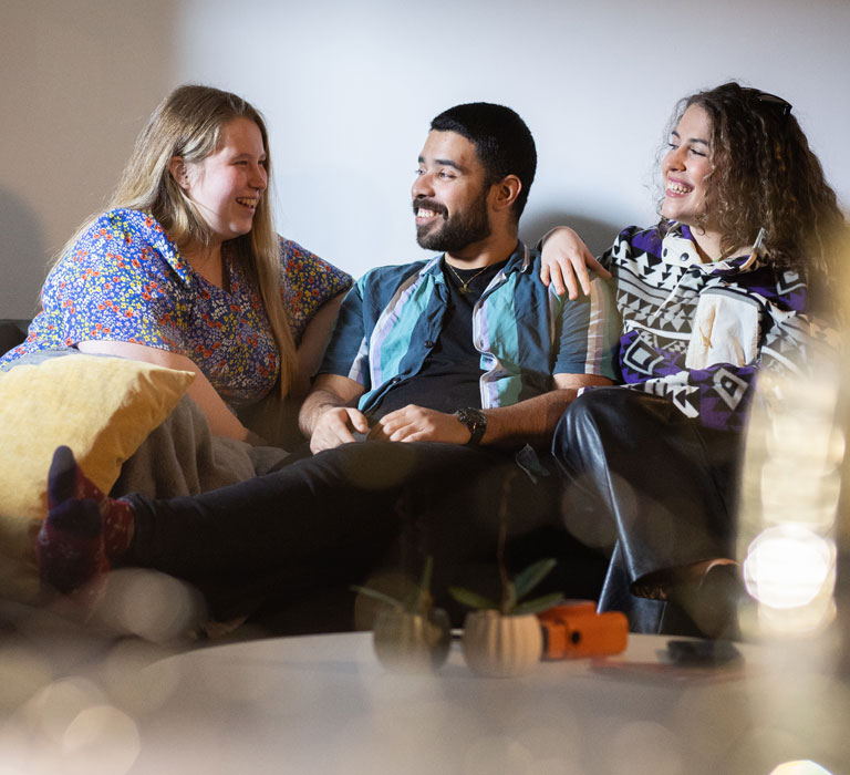 Three students sitting on a sofa smiling and chatting with each other