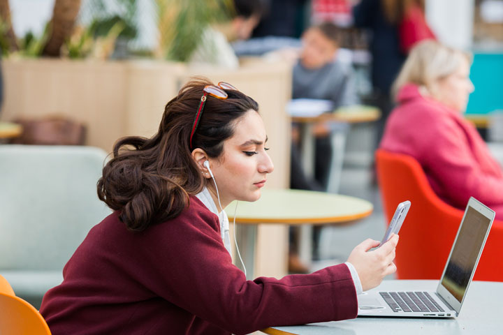 A student sitting at a table in the Richmond building, with a laptop and a mobile phone
