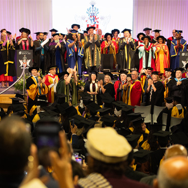 Representatives of the University on stage applauding during a graduation ceremony.