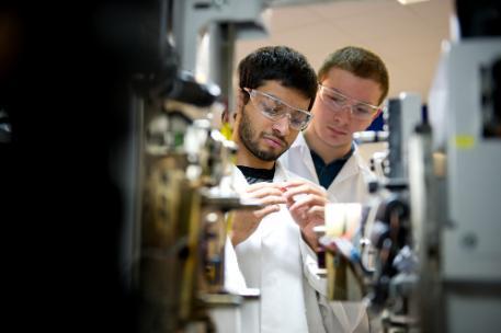 Two students in lab coats wearing goggles