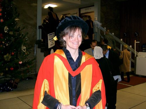 Andrea Cullen, BSc Computing with Management (2000) and PhD Operations and Supply Chain Management (2004) on her graduation day, wearing a red and gold graduation gown and black academic cap.