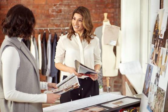 Sonya Bachra-Byrne, MBA, 2023, holding a fashion magazine and speaking to an individual in a fashion studio setting.