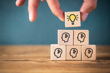 A stack of blocks and a hand picking up a block with a picture of a lightbulb on it.