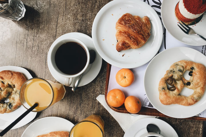 An imaging showing a table of breakfast foods including pretzels, croissants, coffee, water, juice and fruit