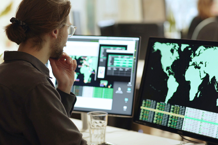 Person looking at two computer monitors. One has a map of the world.