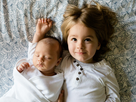 A baby and their toddler sibling lying next to eachother.