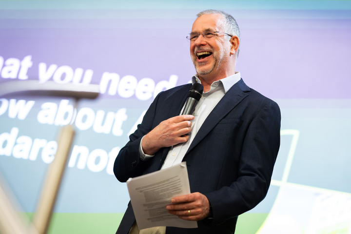 MBA Director, Nick Snowden, smiling and laughing while on stage presenting the MBA Summit 2024.