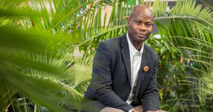 A smartly dressed student sitting down surrounded by plants.