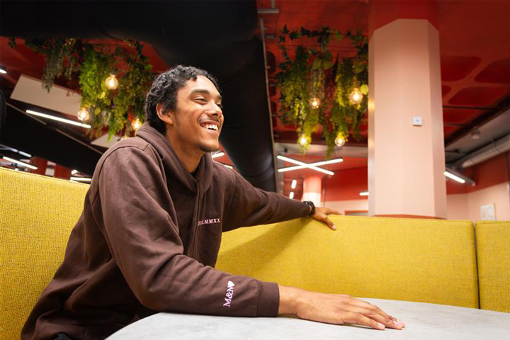 A student smiling while sitting in a booth at the Brew and Co Kitchen in Student Central