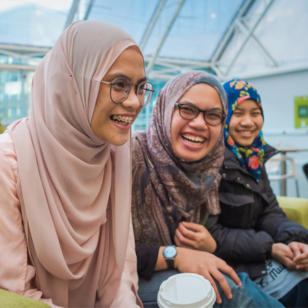 Three students sat together and laughing in the Atrium