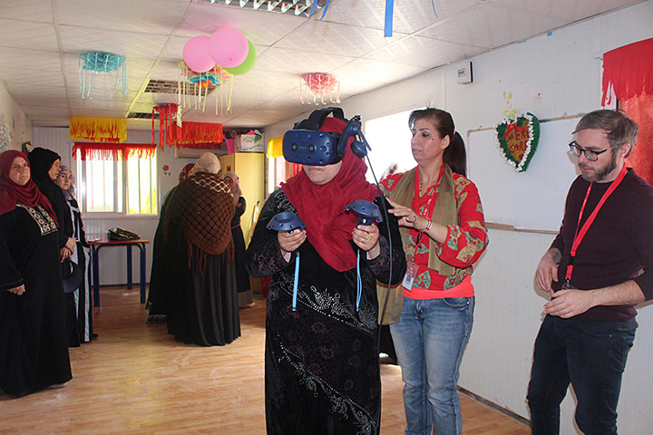 A refugee wearing a VR headset while a person helps guide them.