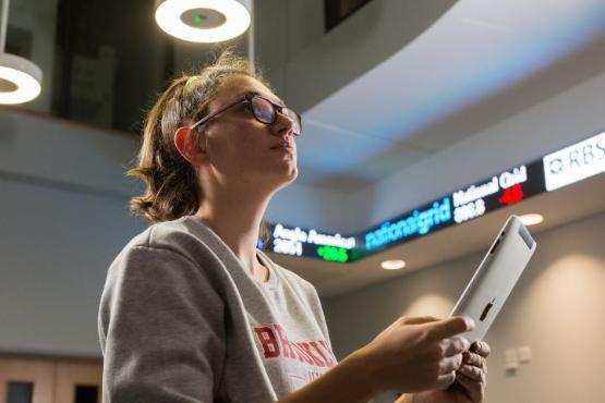 Student in University room with 'tickertape' stock trading display in background