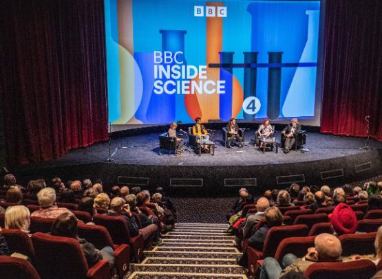 FIve people sat on a stage with microphones with the audience in the foreground