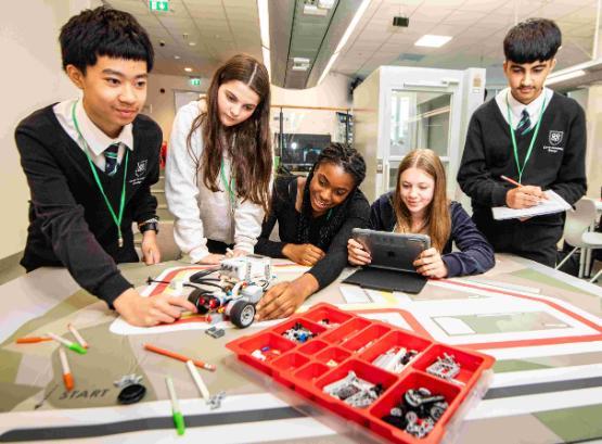 Five students stood up and sat down behind table with small robot made out of Lego bricks on it