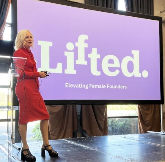 Person stands next to giant projector screen while giving a presentation at a conference