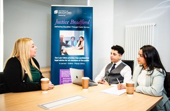 Three people sat at wooden table talking with Justice Bradford banner in background