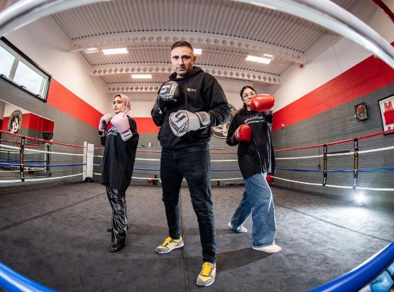 Two students in a boxing ring with professional boxer Tasif Khan