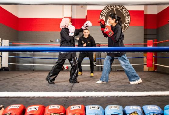 Two students in a boxing ring with professional boxer Tasif Khan