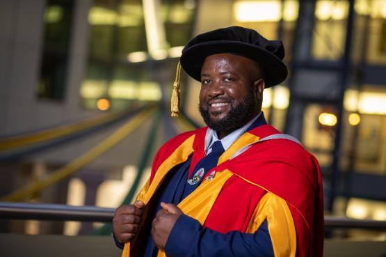 Elgidius Edgar Bwinabona Ichumbaki stands in gown and hat in University of Bradford Atrium