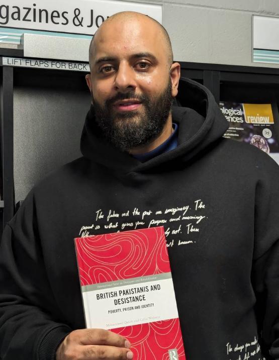 Staff member wearing black hoodie holds book