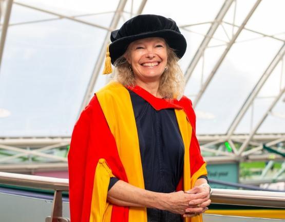 A person stands up and poses for photo in graduation gown and headware