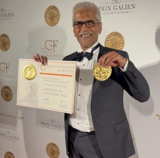 Person in suit on award ceremony red carpet holding up awards